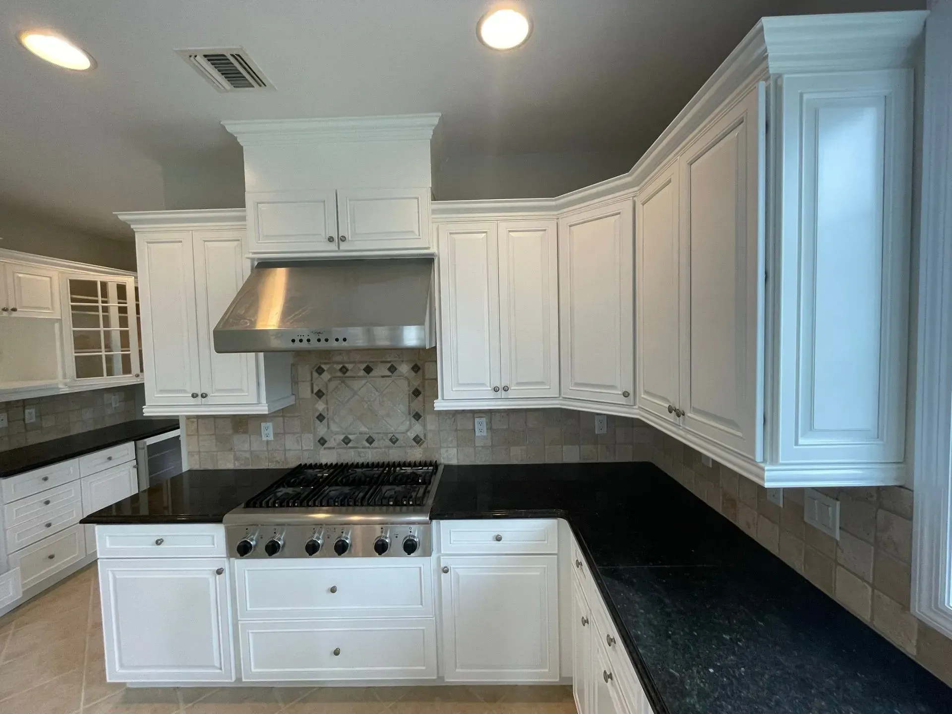 White kitchen cabinets with black countertops and a stainless steel range hood.