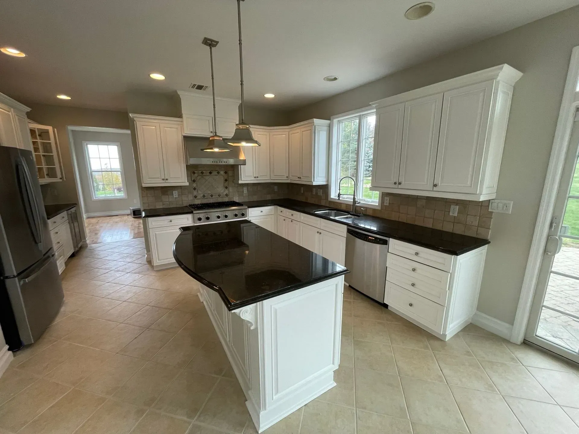 White kitchen with black countertops, island, stainless steel appliances, and tile floor.