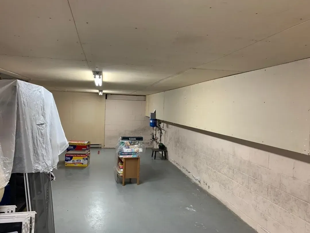 Basement room with gray floor, white walls, and a few boxes and items on a table.