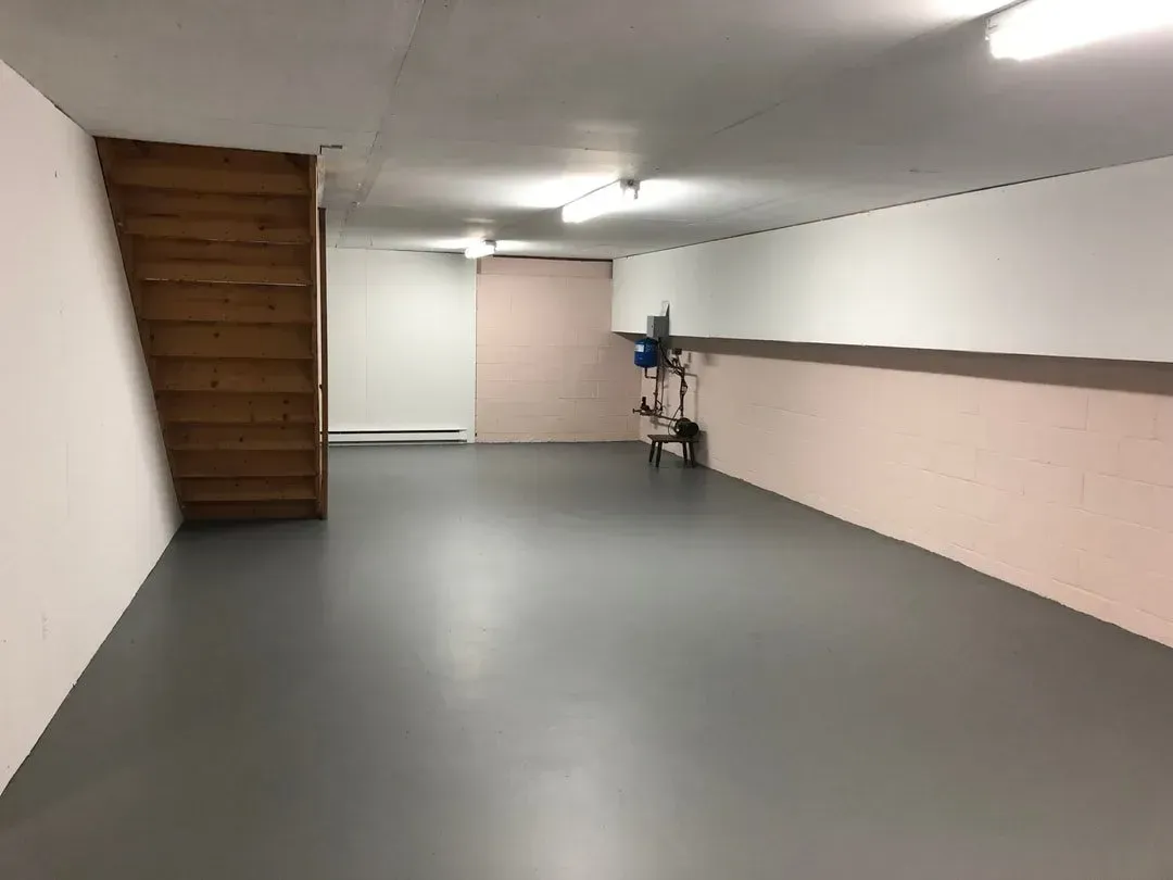 Empty basement with gray floor, wooden stairs, and white and pink walls.