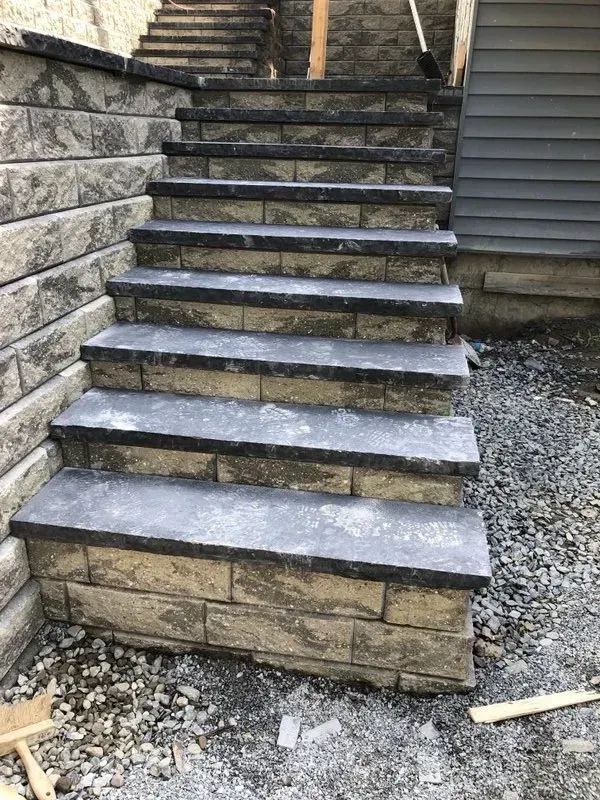 Stone staircase with retaining wall, leading upwards beside a building. Gray steps, tan walls.