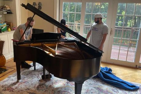 A group of people are moving a piano in a living room.