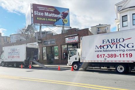 Two moving trucks are parked on the side of the road in front of a building.