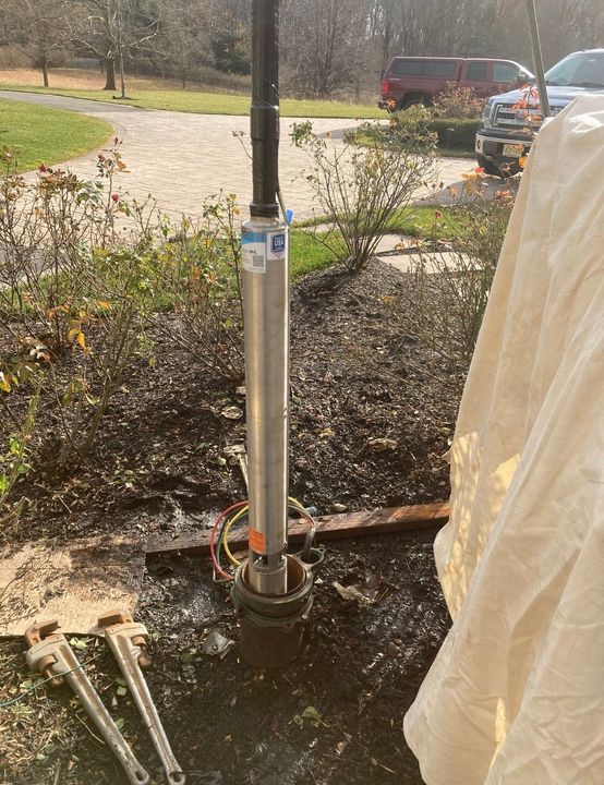 Metal pole being installed in a muddy yard beside a walkway, with a white protective cover nearby.