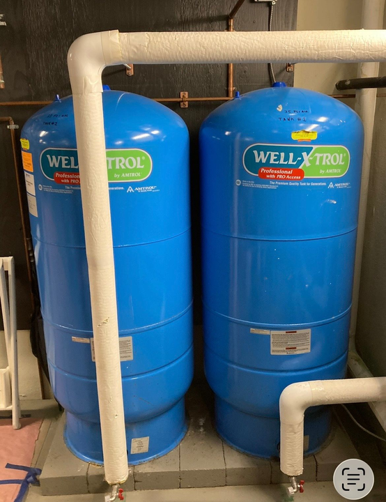 Two blue Well-Flow tanks connected by white pipes in a utility room