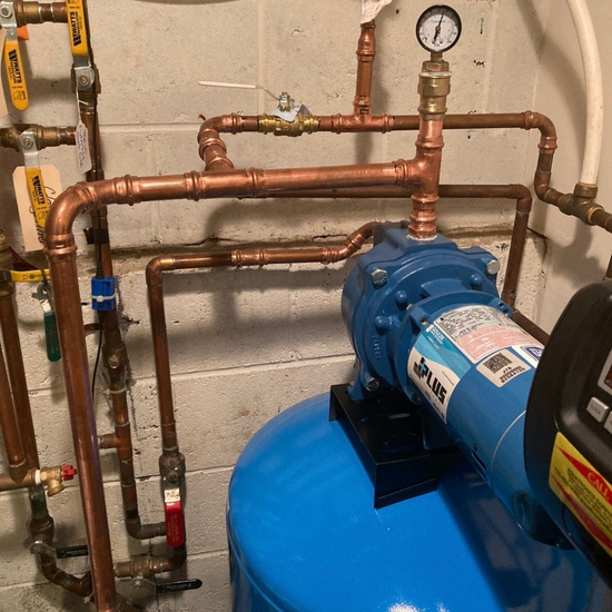 Copper pipes and a pressure gauge above a blue water tank and pump in a utility room