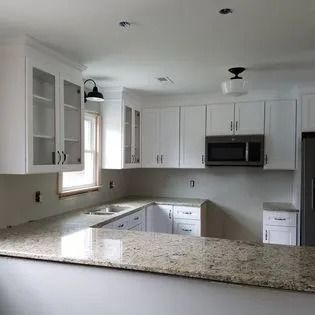 A kitchen with white cabinets , granite counter tops , stainless steel appliances and a window.