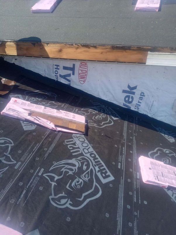 Overhead view of roofing underlayment, pink insulation, and wooden boards on a roof during construction.