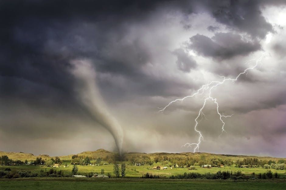 Tornado descends over a green landscape as lightning strikes amidst dark storm clouds.