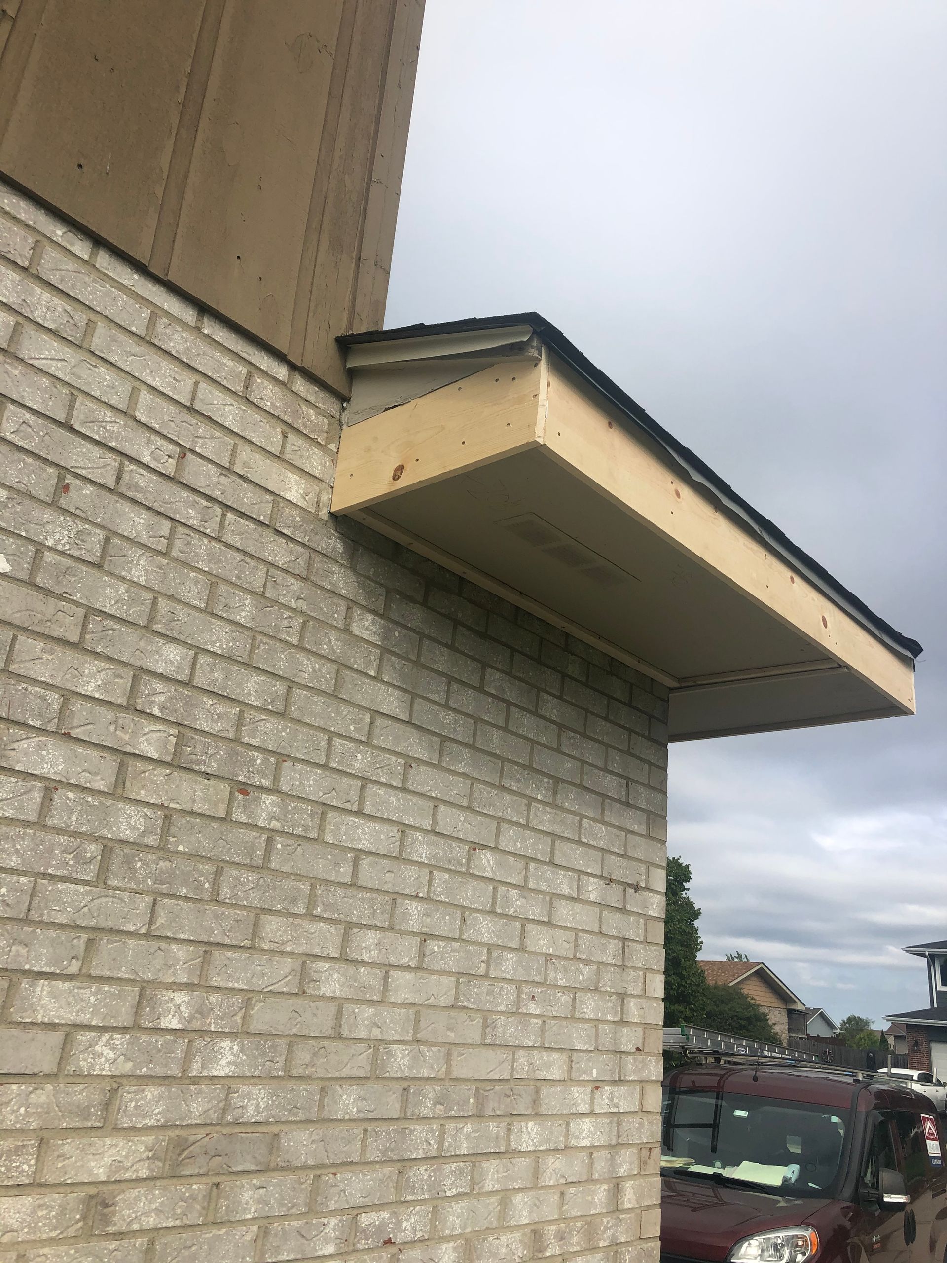Brick building with overhanging roof, supported by angled boards. Cloudy sky overhead.