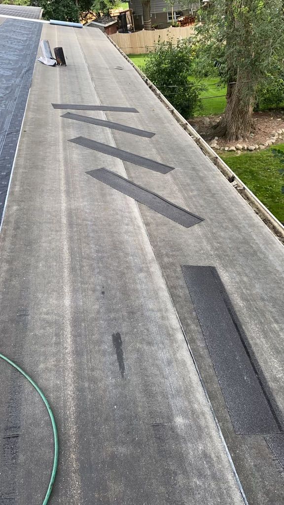 Flat roof with black repair patches; a hose and some debris are also visible.