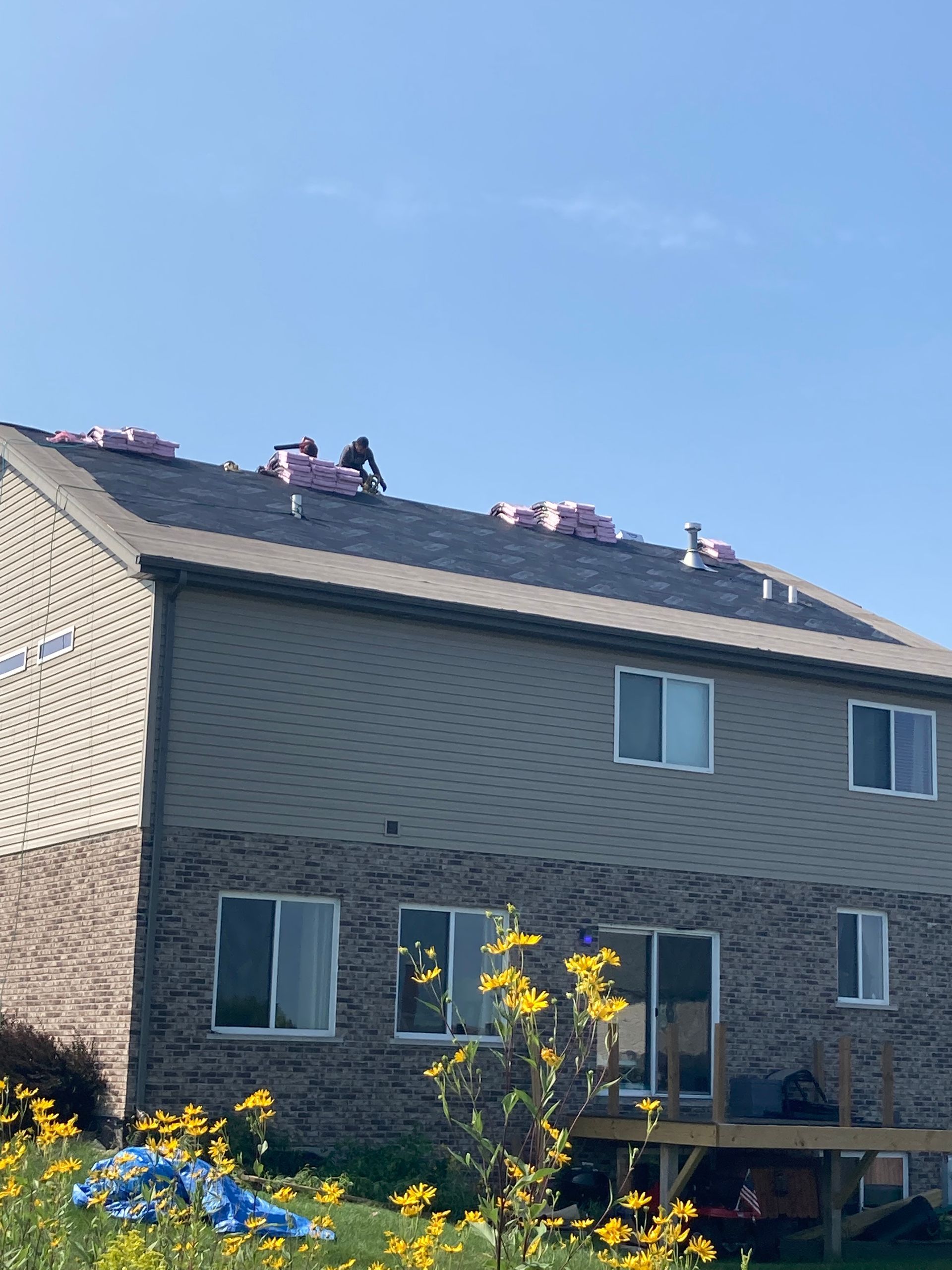 Roofers working on a two-story home, surrounded by shingles and insulation. Blue sky backdrop.