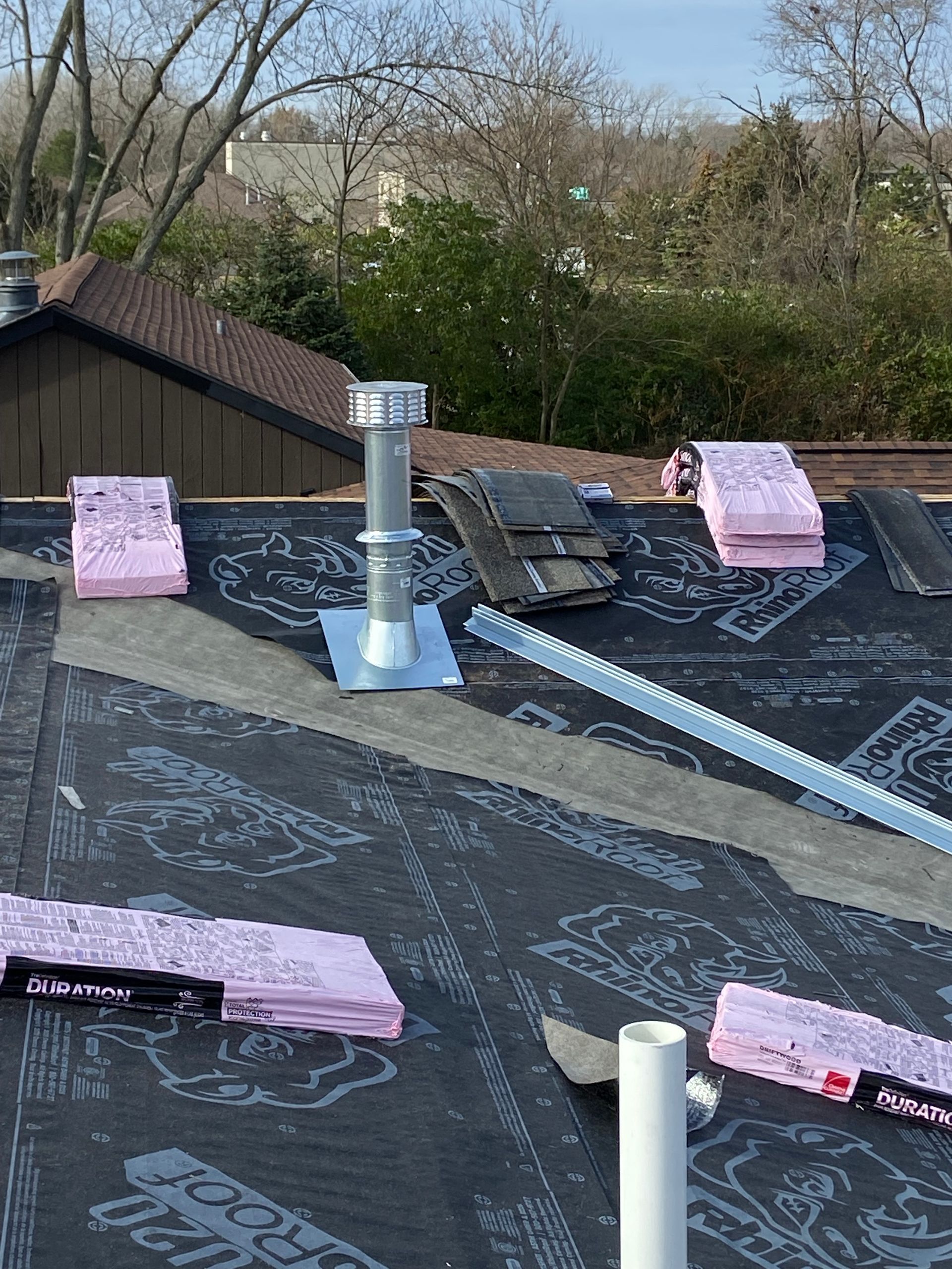 Roof with insulation, vent pipe, and roofing materials; trees and building in the background.