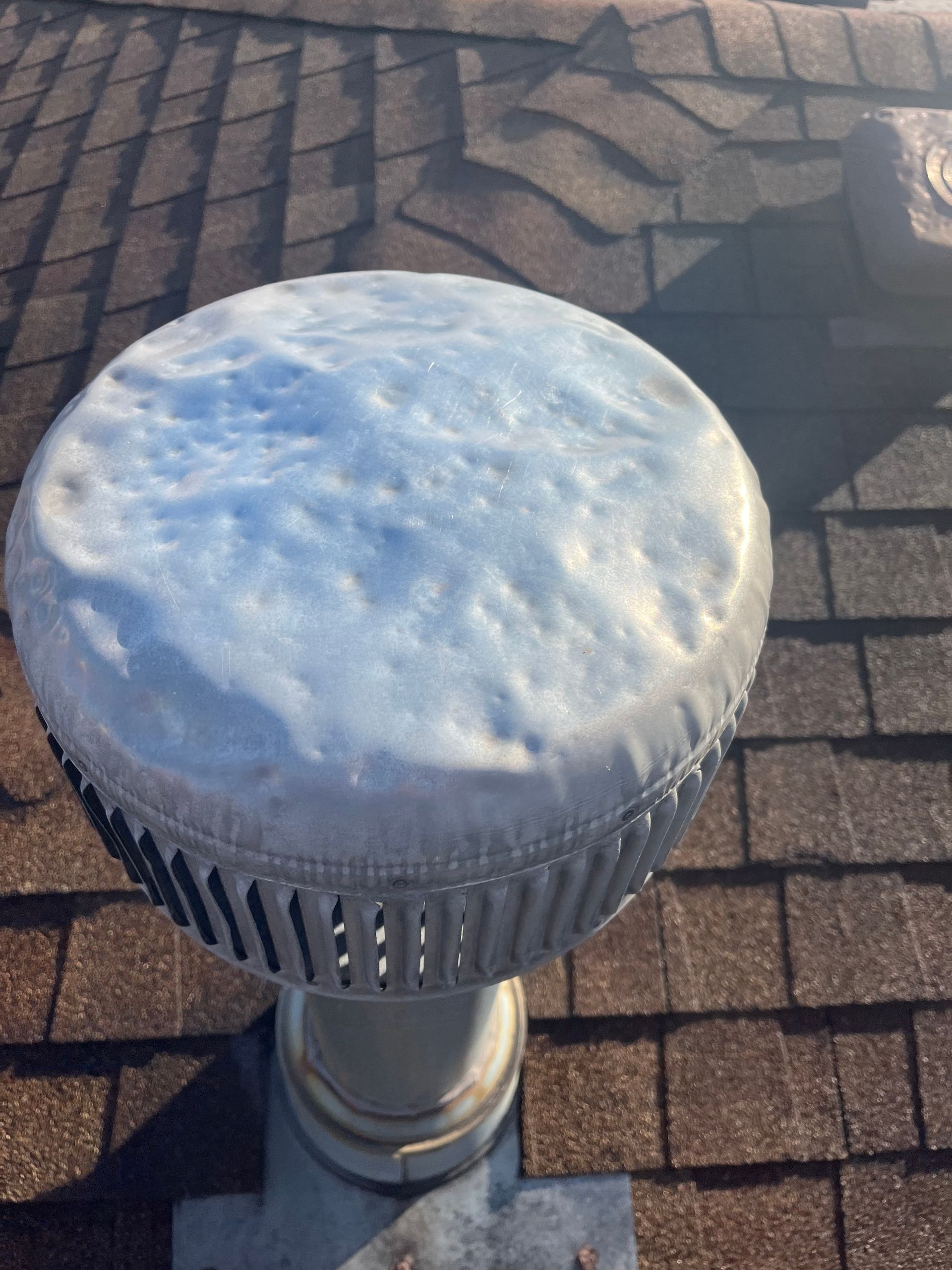 Close-up of a silver vent cap covered in white frost on a shingled roof.