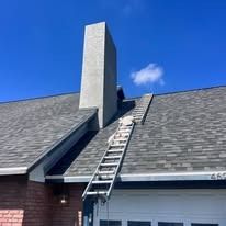 Person on a ladder repairing a chimney on a house with a blue sky.