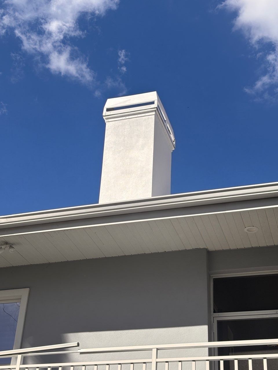 White chimney on a building roof against a blue sky with clouds.