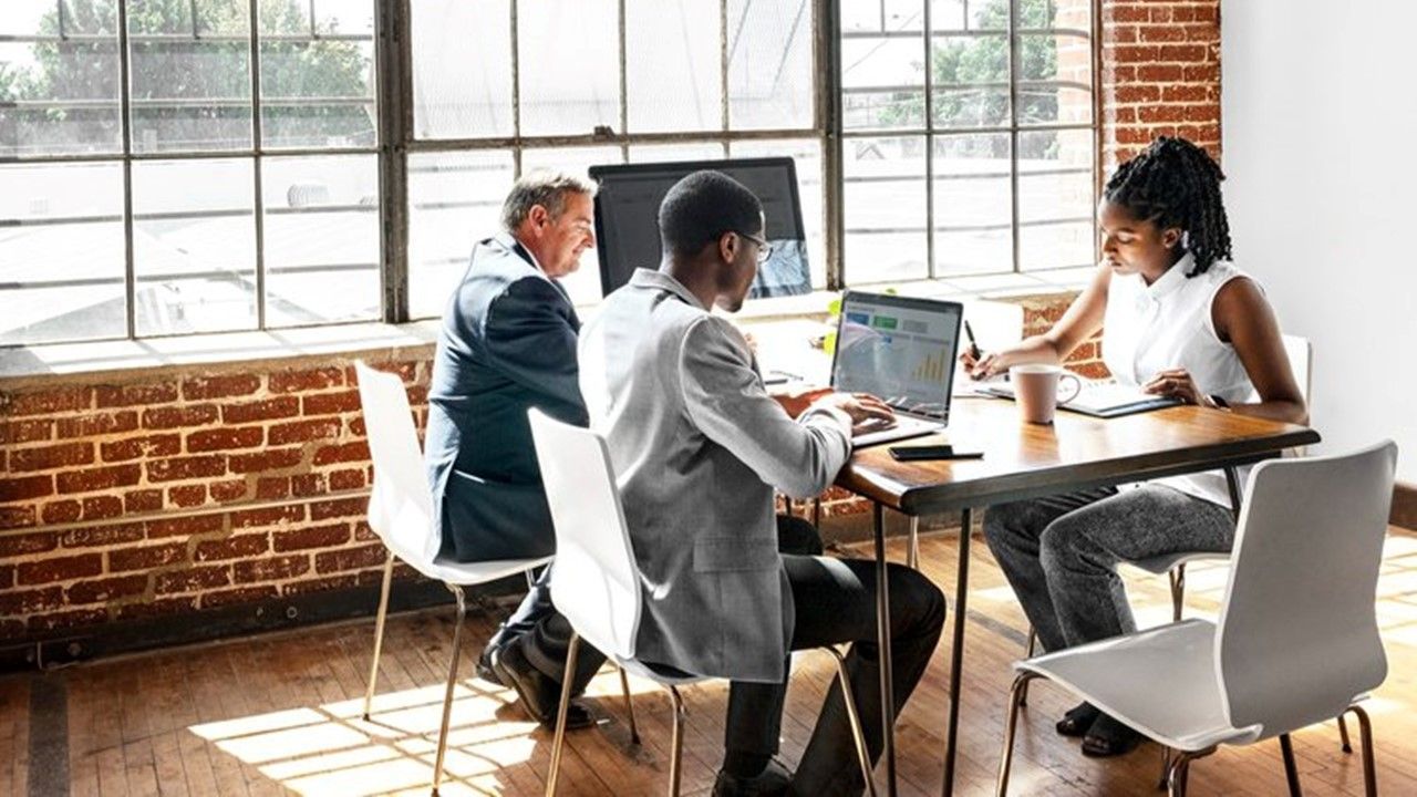 A group of people are sitting around a table with laptops.