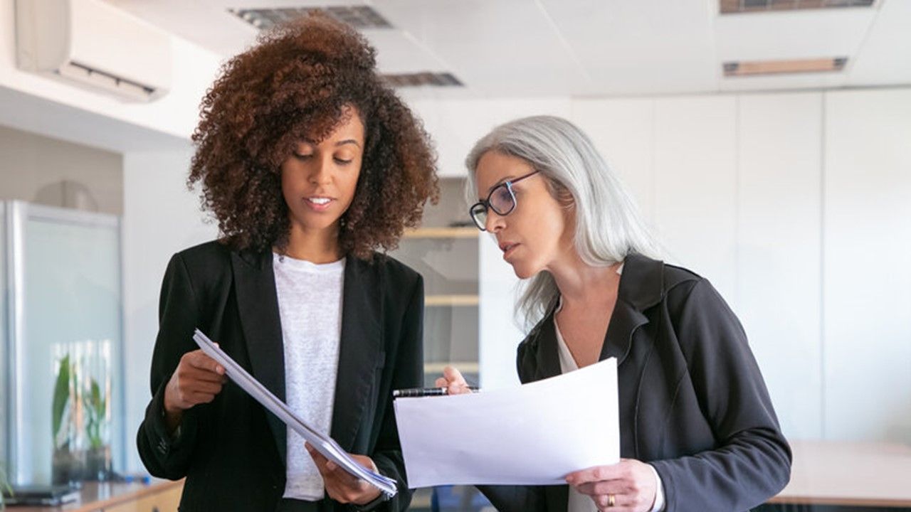 Two women are looking at a piece of paper in an office.