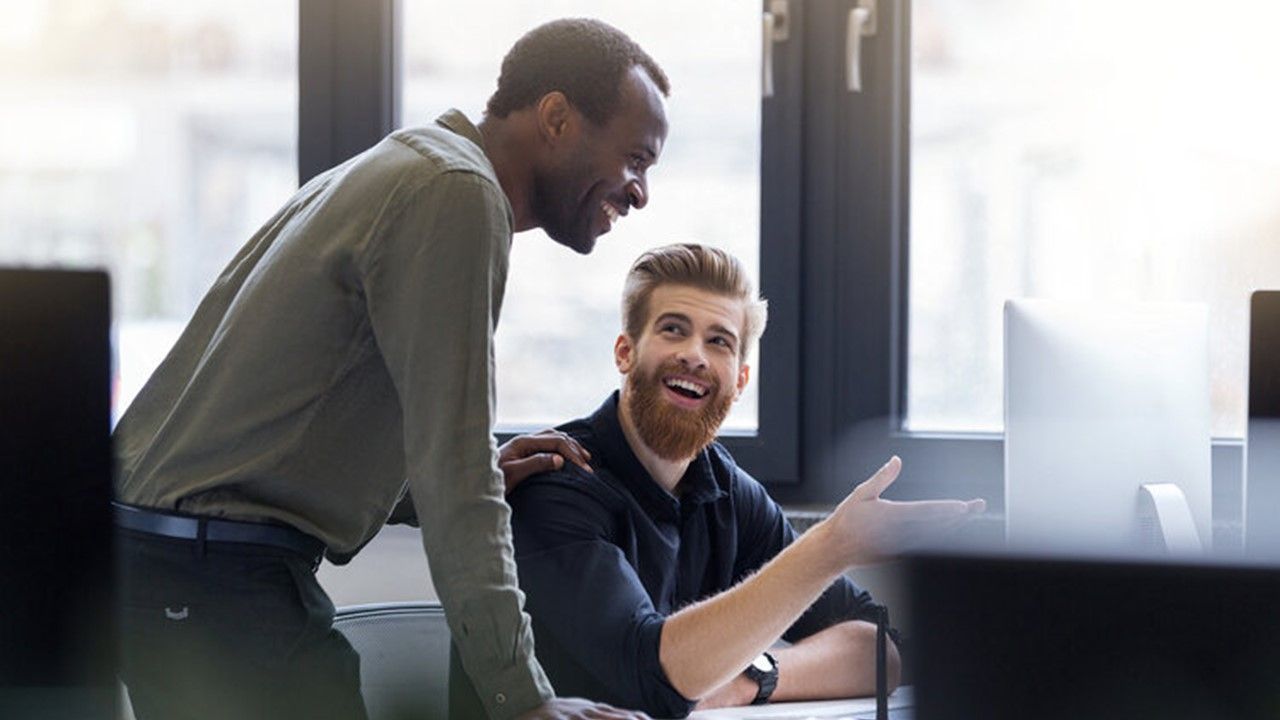 Two men are standing next to each other in front of a computer.