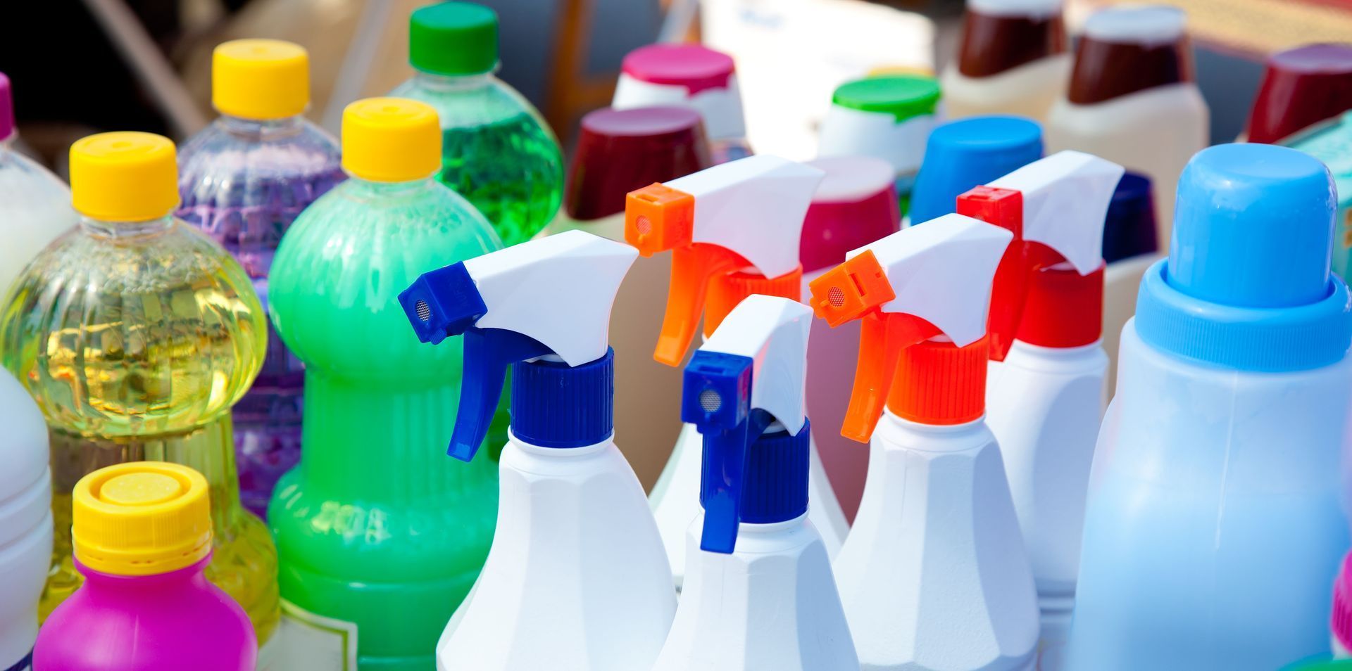 Bottles of cleaning products with colorful liquids and spray nozzles.