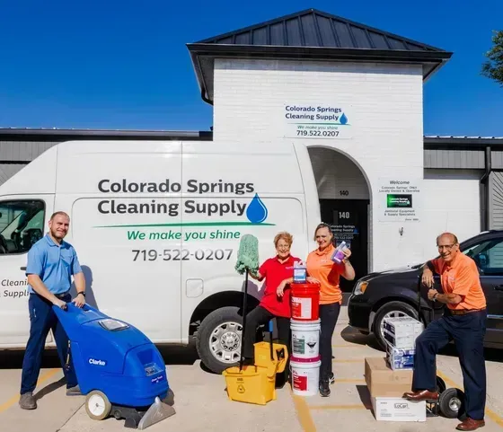 Four people standing with cleaning supplies and equipment in front of a Colorado Springs Cleaning Supply van and building.