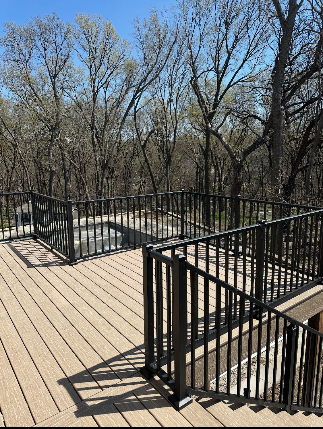 Deck with black metal railing, overlooking a wooded area on a sunny day.