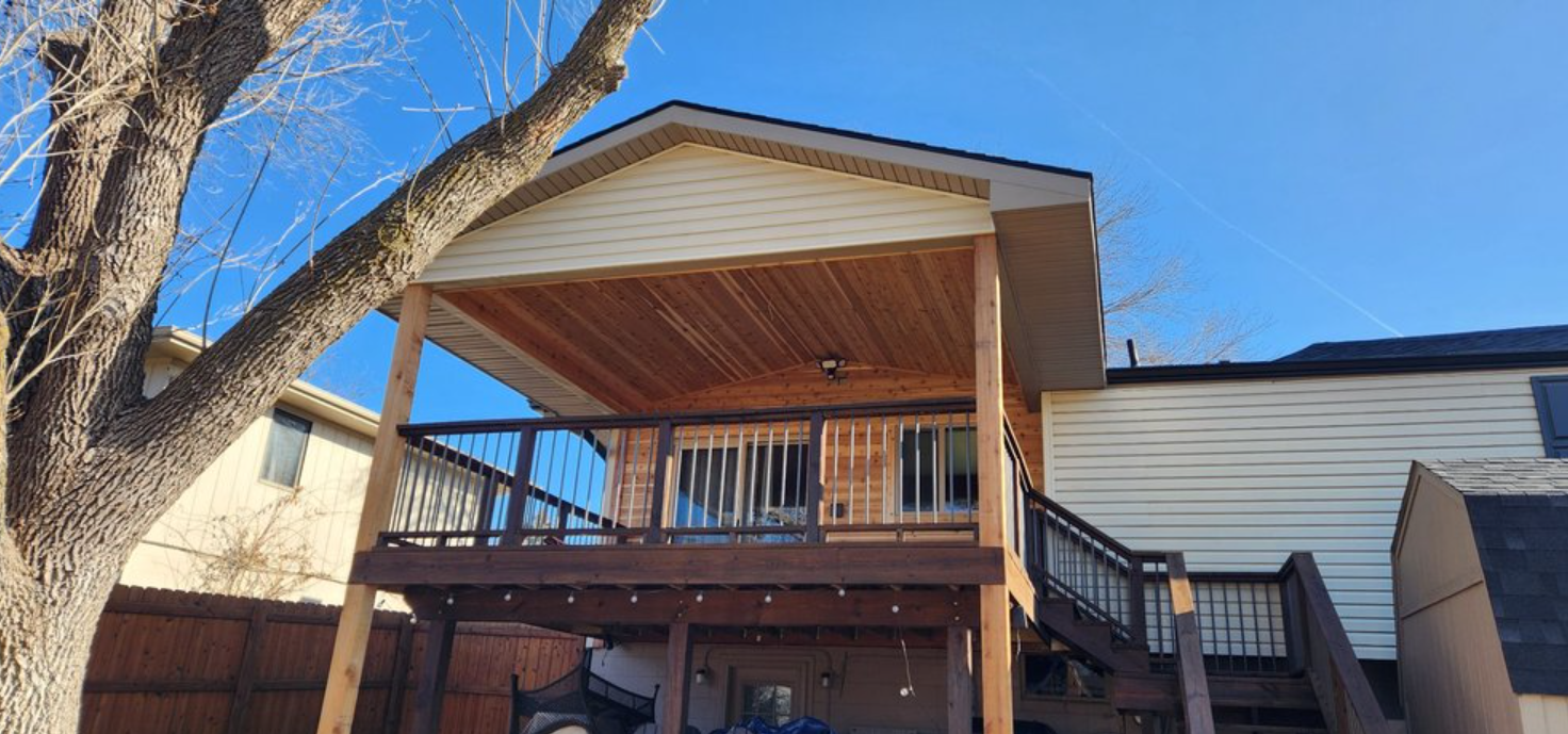 Back of a house with a wooden deck and porch, blue sky overhead.