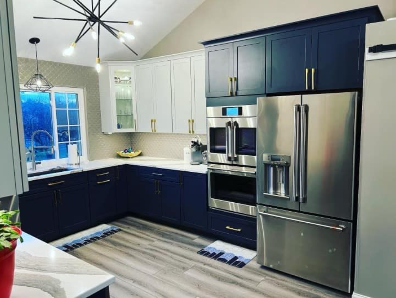 Modern kitchen with navy and white cabinets, stainless steel appliances, and wood-look flooring.