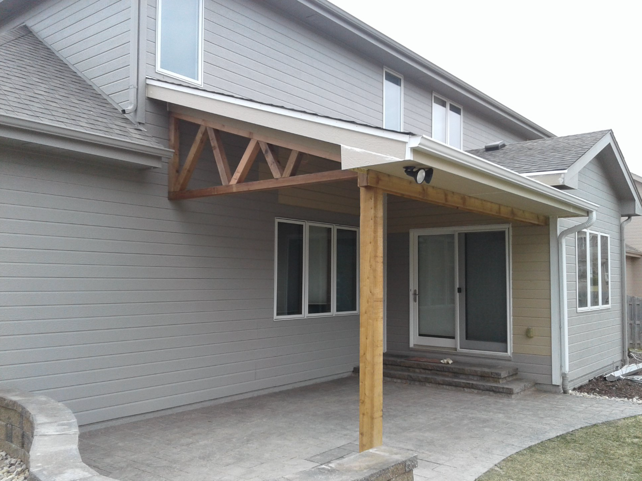 Patio extension with wooden supports attached to a light gray house.