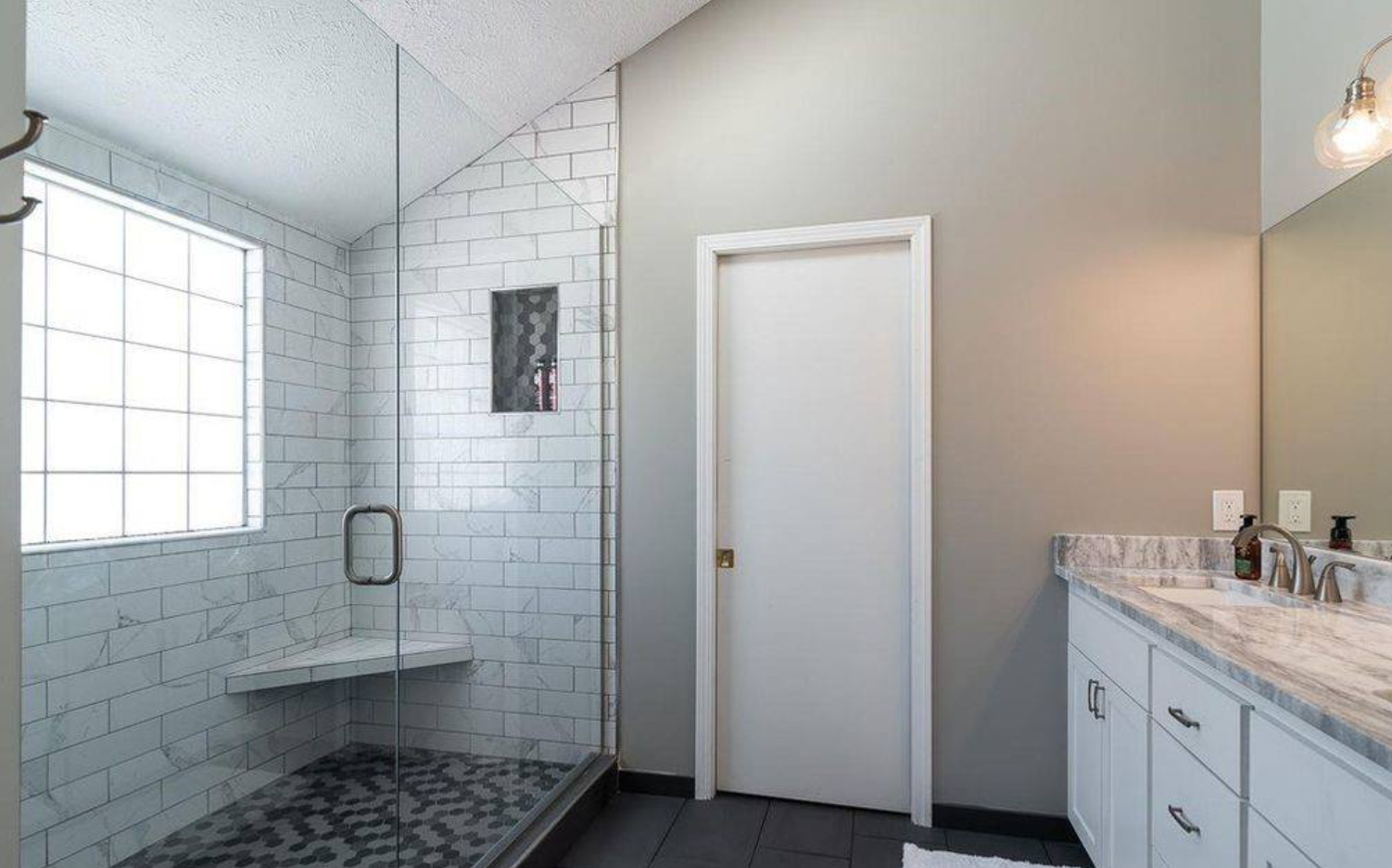 Bathroom with a white tiled shower, glass door, white vanity, and gray walls.