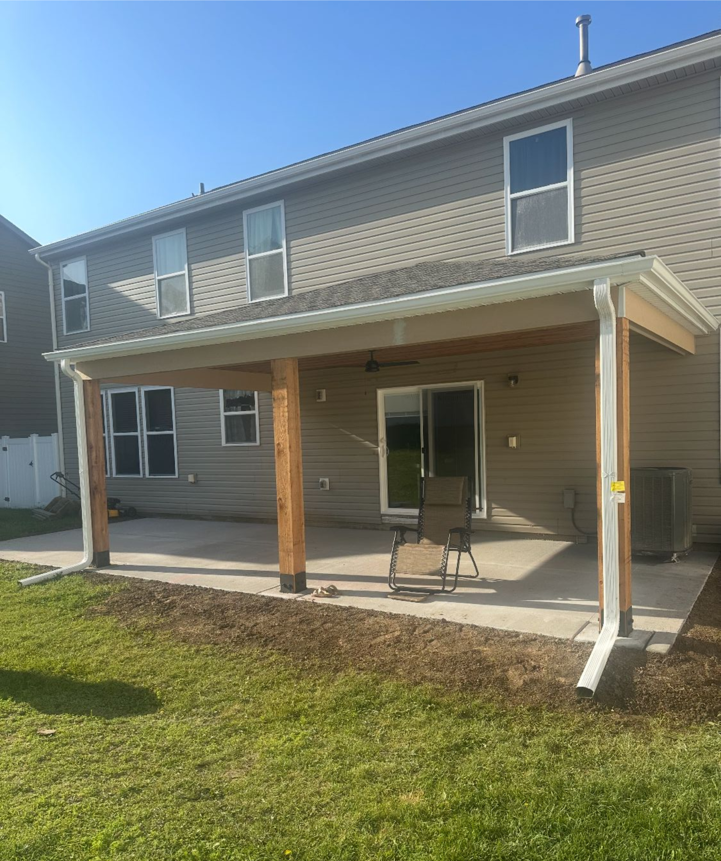 A backyard patio with a covered roof, a chair, and a grassy yard. Gray siding house.