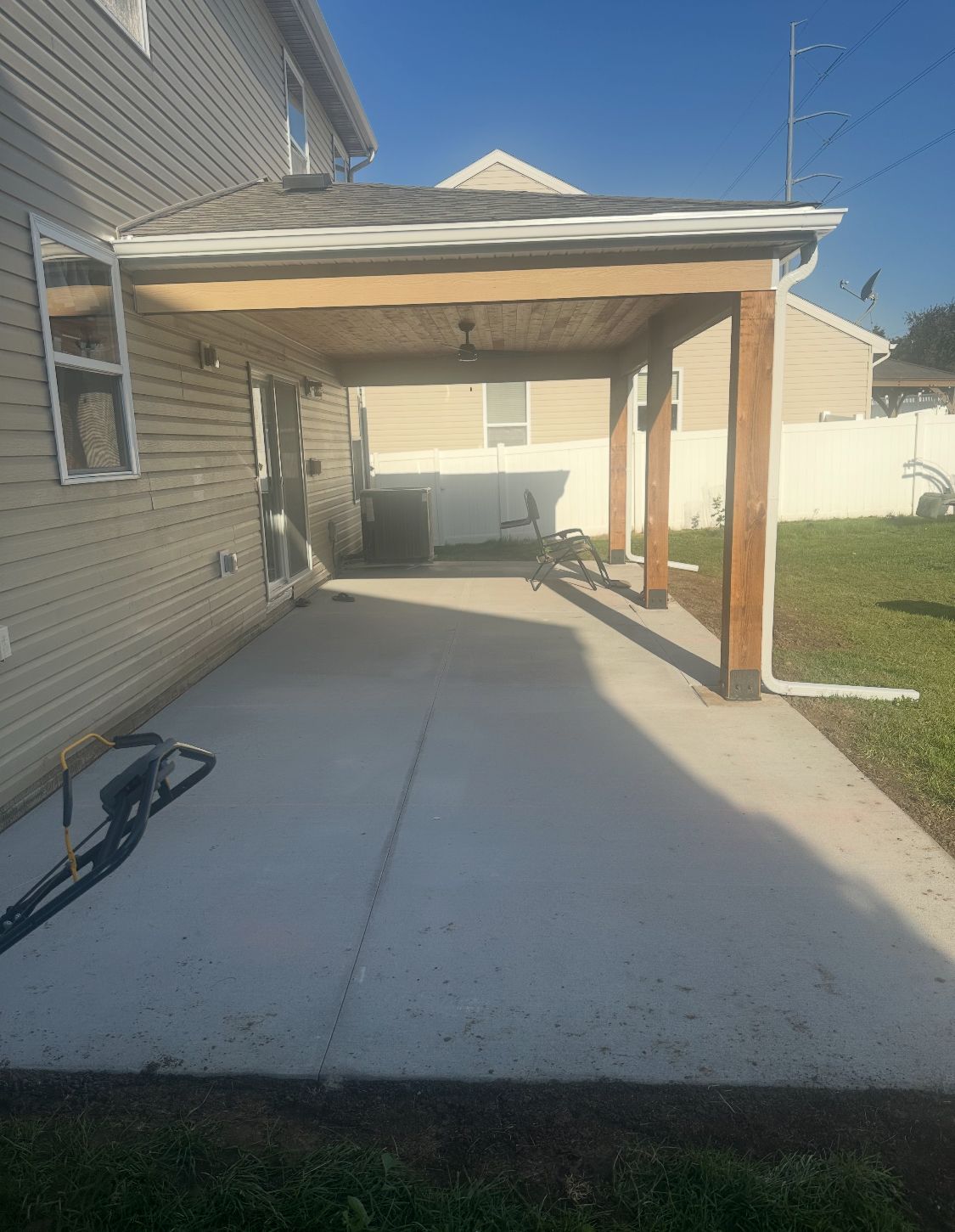 Concrete patio with attached covered porch, brown beams, extending from a two-story house.