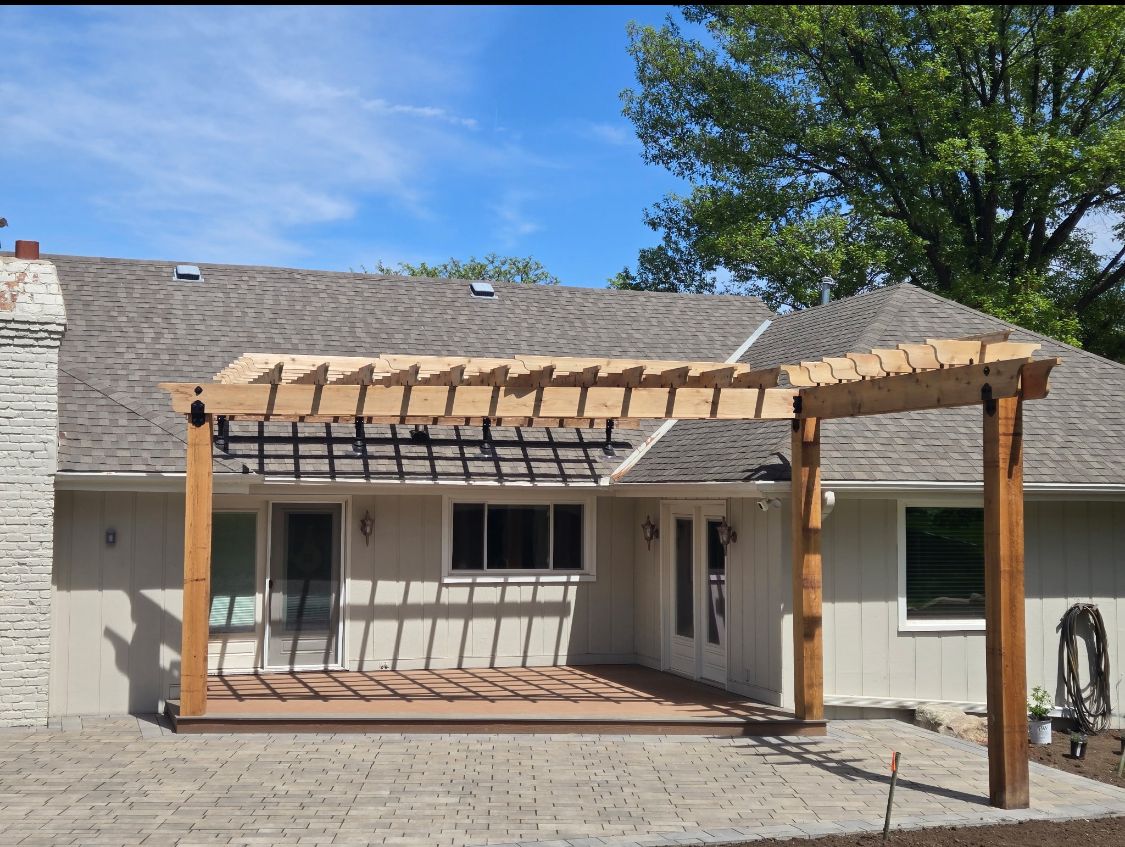 Wooden pergola over patio attached to a house with light siding and a brick chimney.
