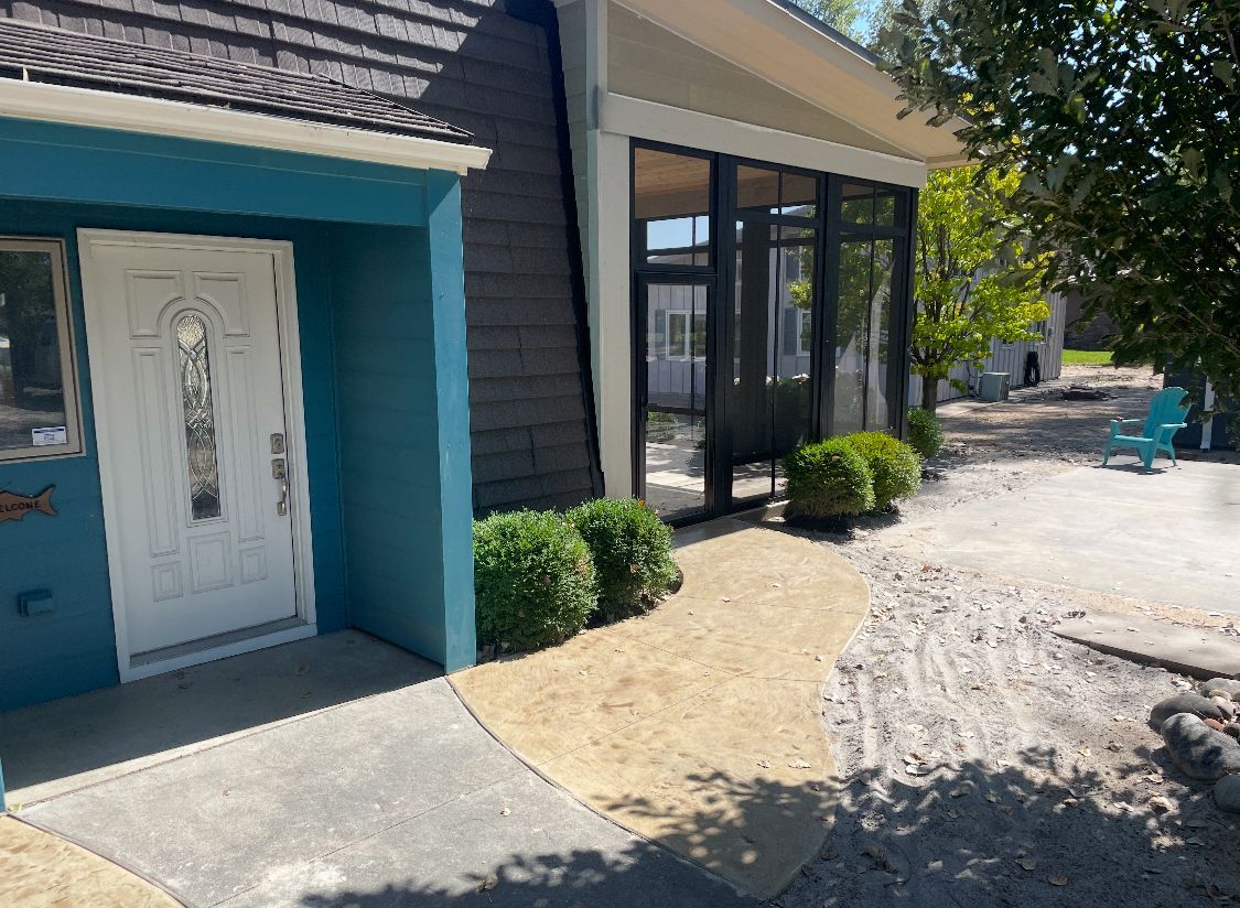 Blue and gray house with white door, screened porch, walkway with bushes.