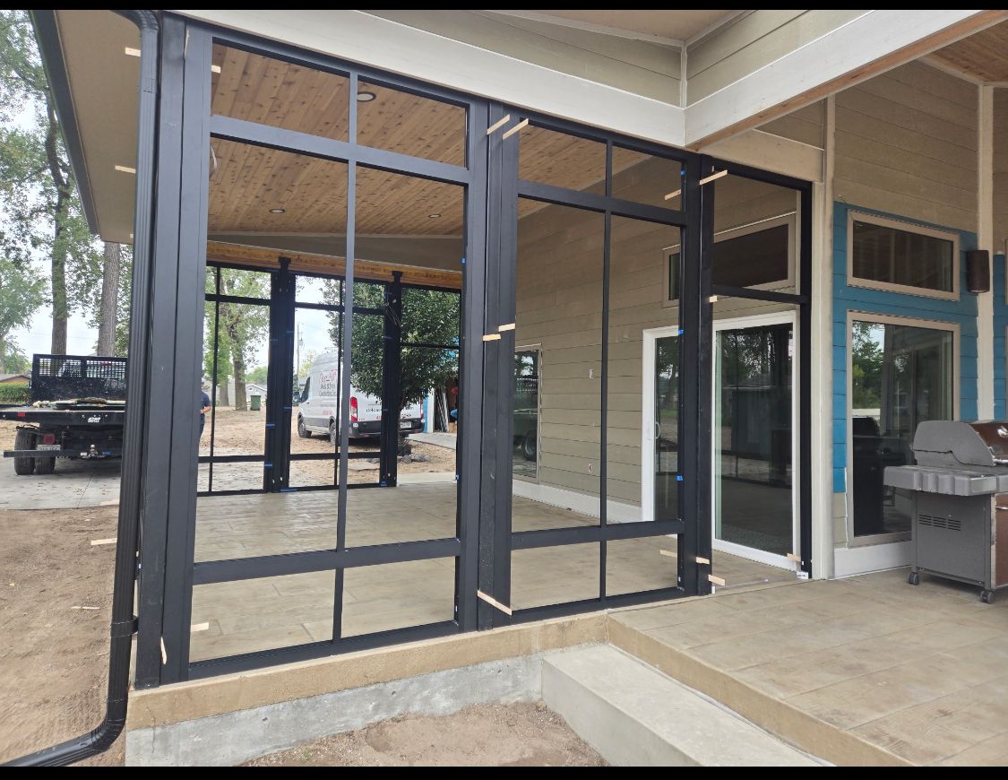 Black-framed glass doors and windows on a porch, leading to an interior space. Construction site setting.