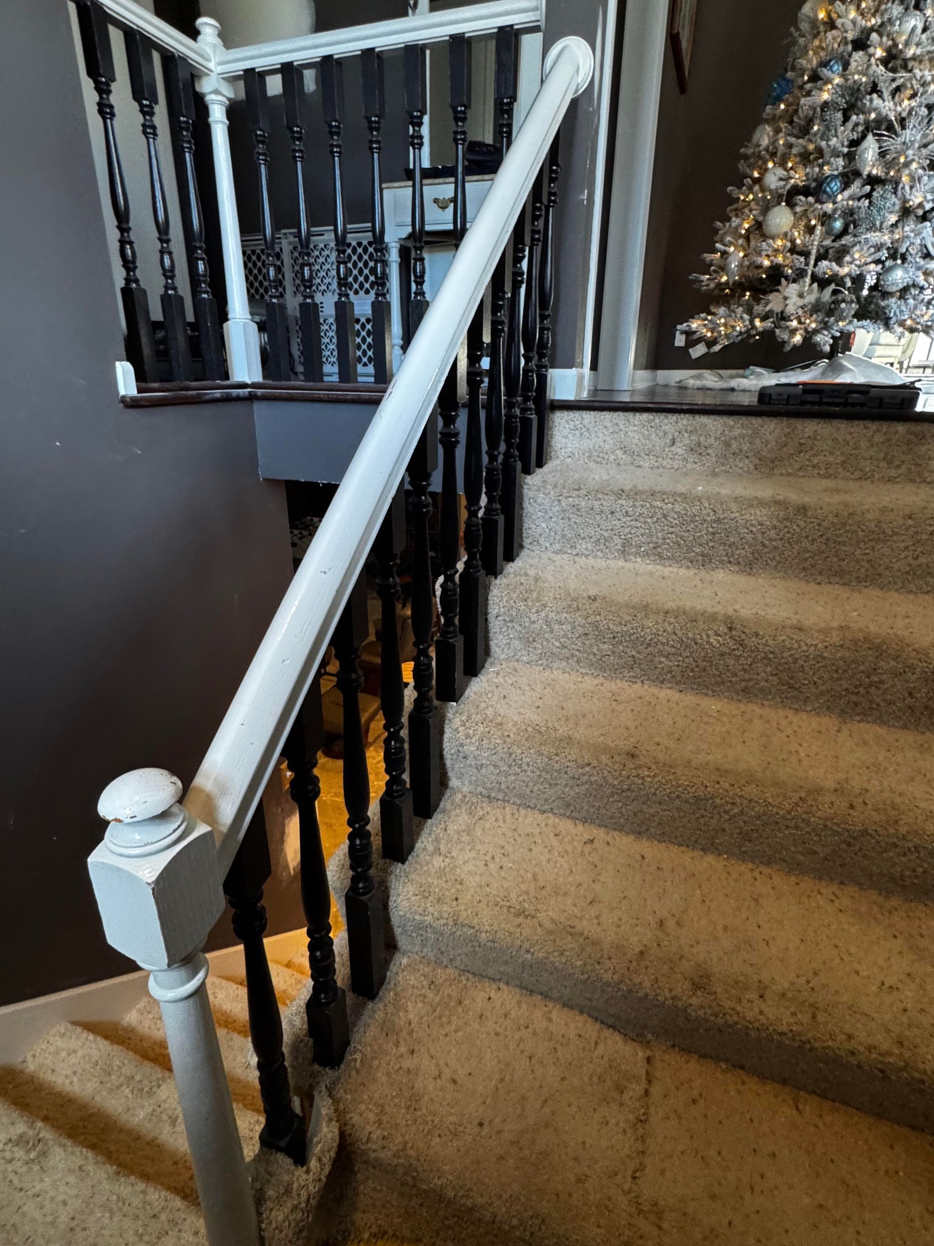 Staircase with carpeted steps and black spindles, white handrail, and brown walls.