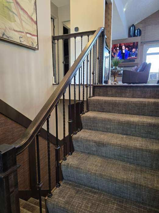 Staircase with gray carpet steps, dark wood handrail, and wrought iron balusters. The living room is visible in the background.