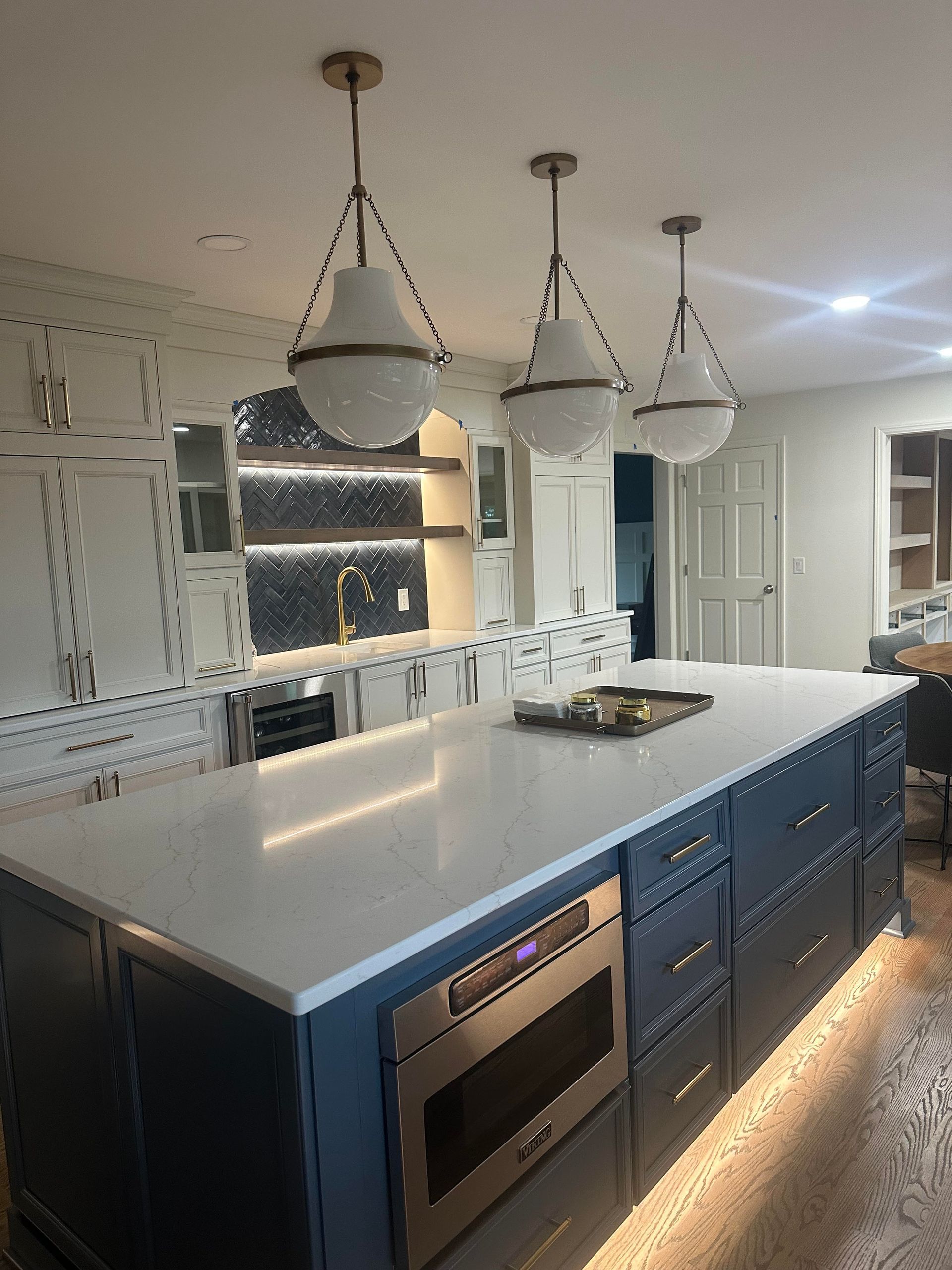 Modern kitchen with a blue island, white countertops, and three hanging pendant lights.