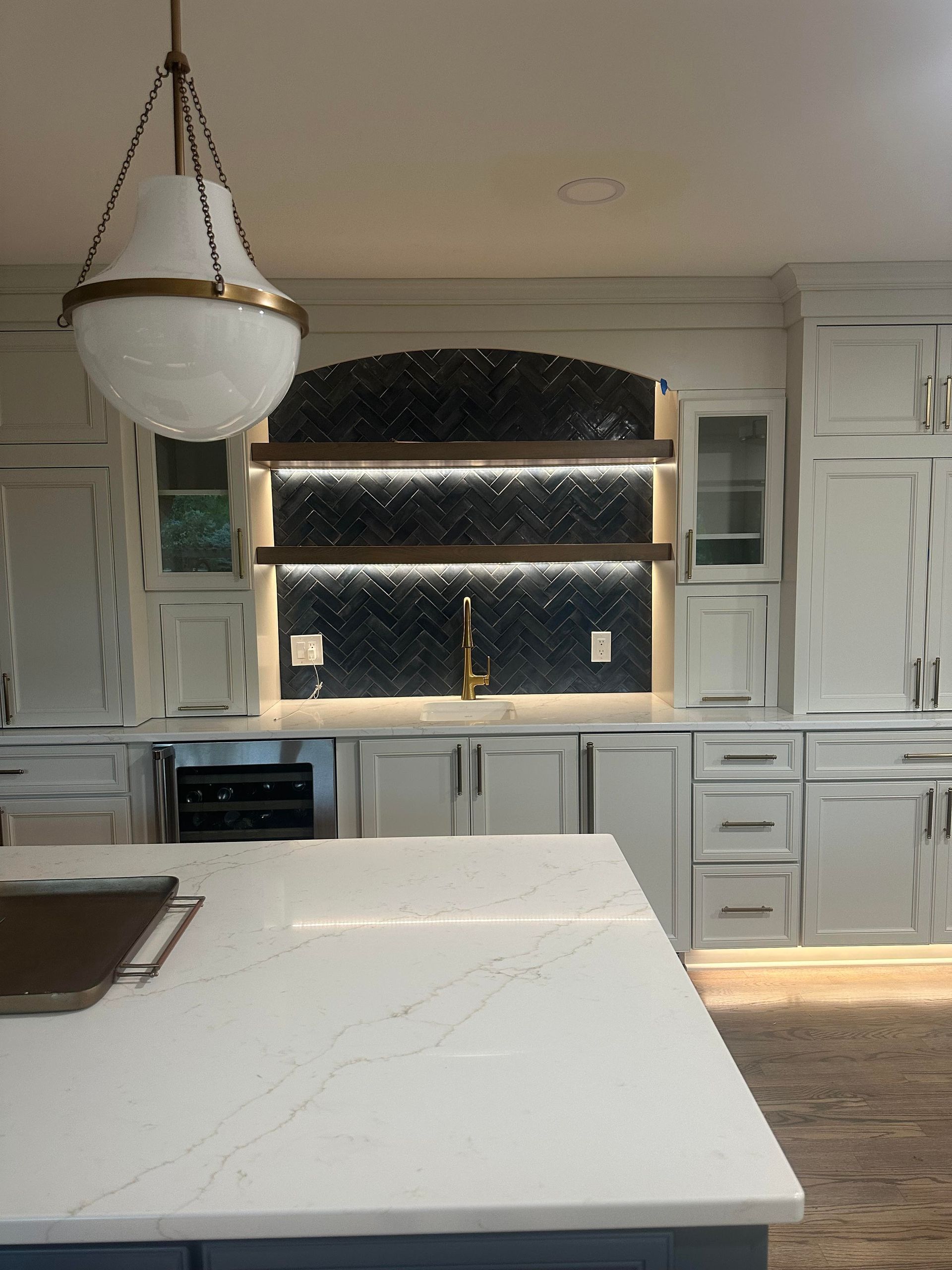 Kitchen with white cabinets, dark tile backsplash, and hanging globe light.