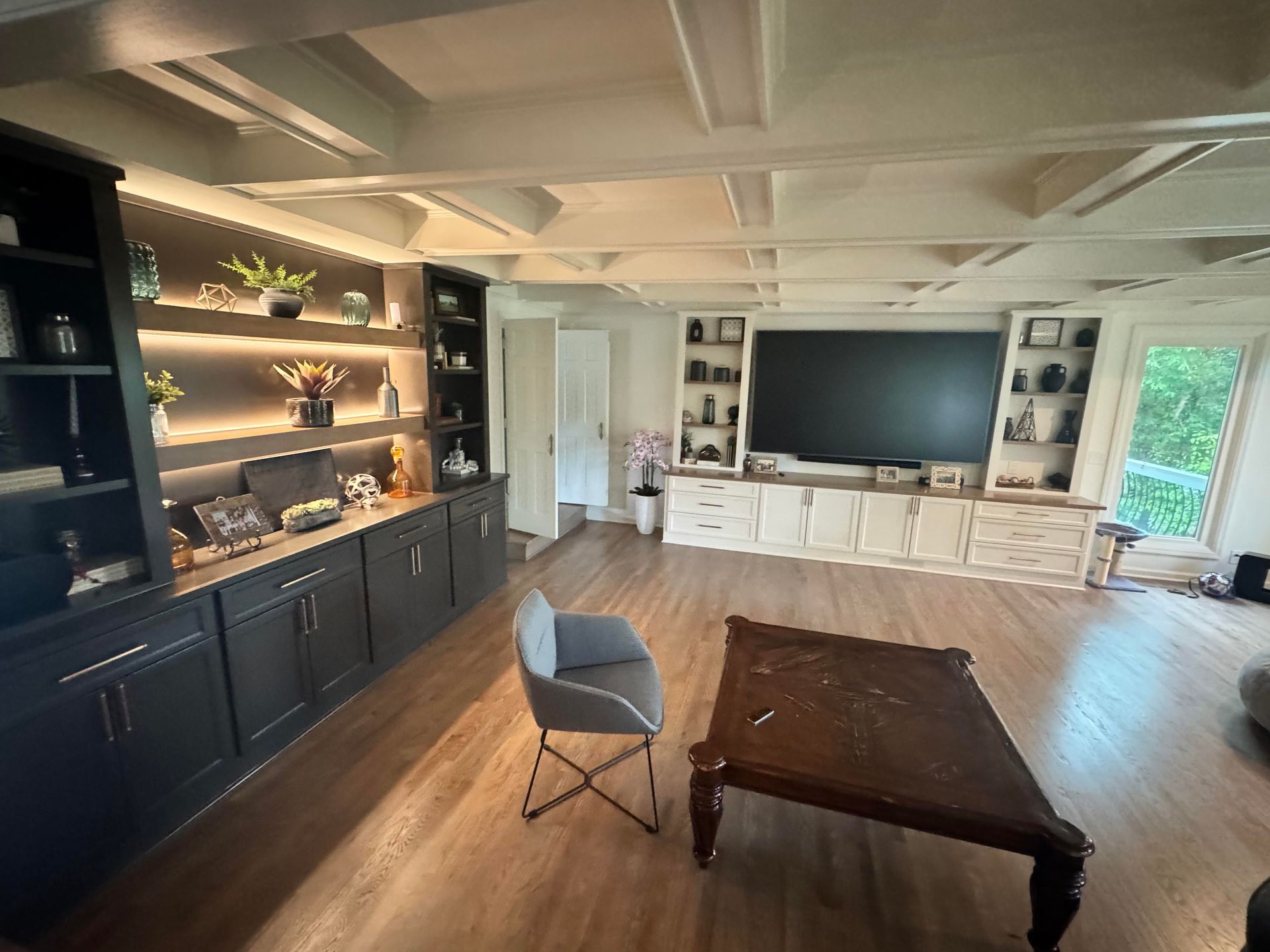 Living room with built-in cabinetry, TV, seating, and decorative items. Bright space with wooden floors.
