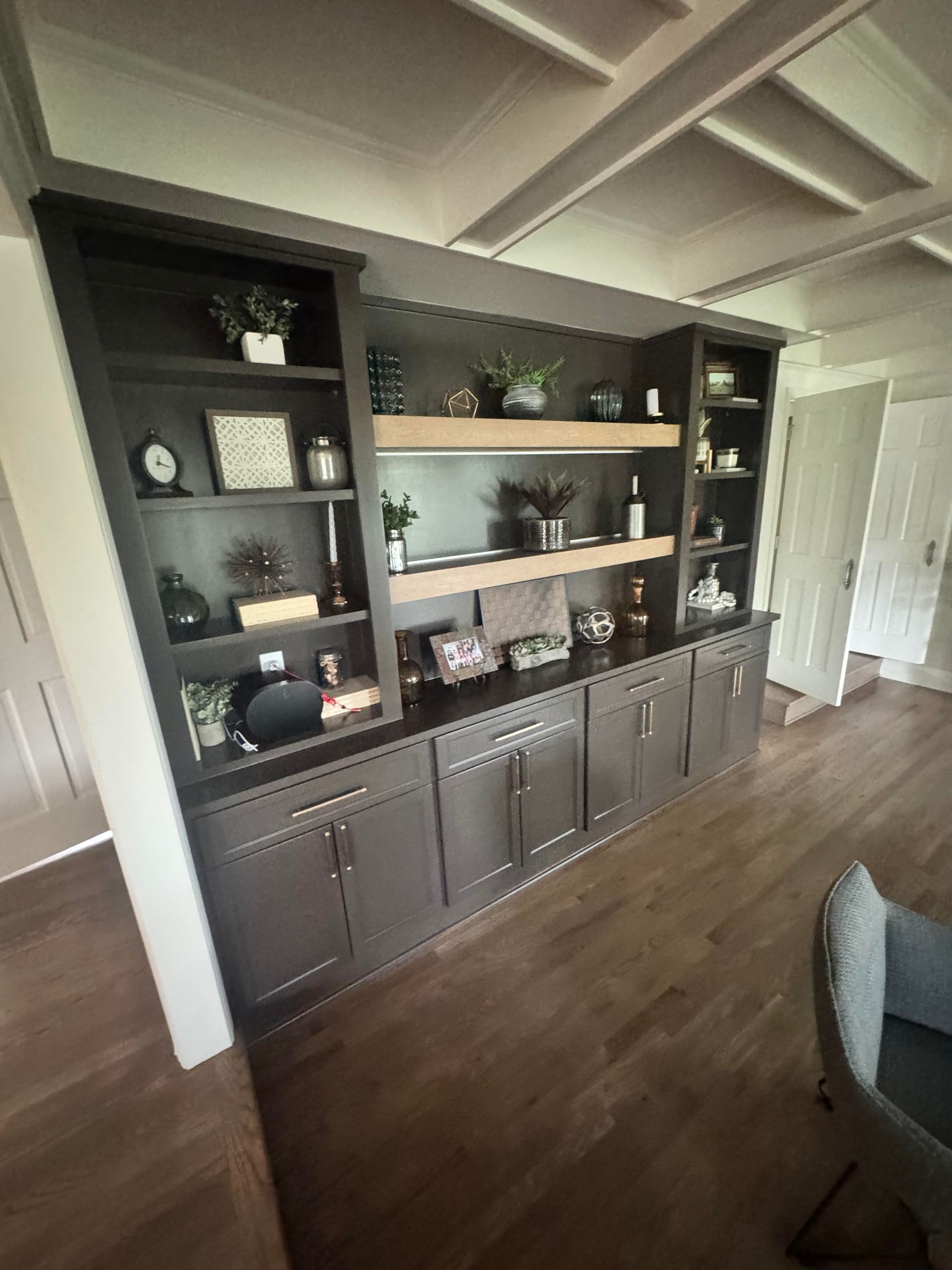 Dark gray built-in cabinet with open shelving, filled with decor, above a closed cabinet base. Beige shelving.