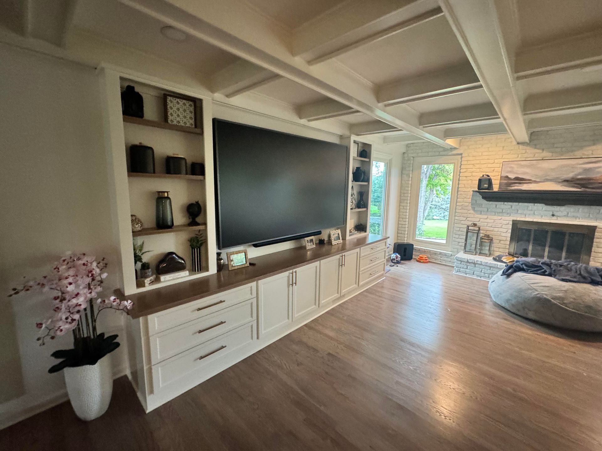 Living room with built-in entertainment center, fireplace, hardwood floors, and exposed ceiling beams.