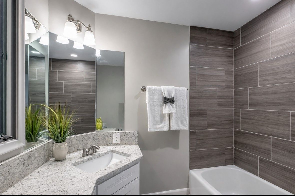 Modern bathroom with gray tile shower, white vanity, mirror, and chrome fixtures