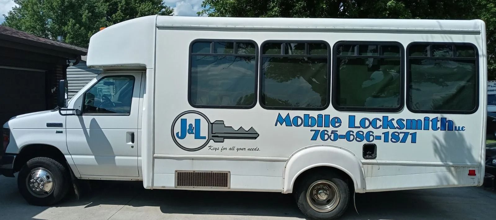 White mobile locksmith van with blue lettering and logo parked outdoors.
