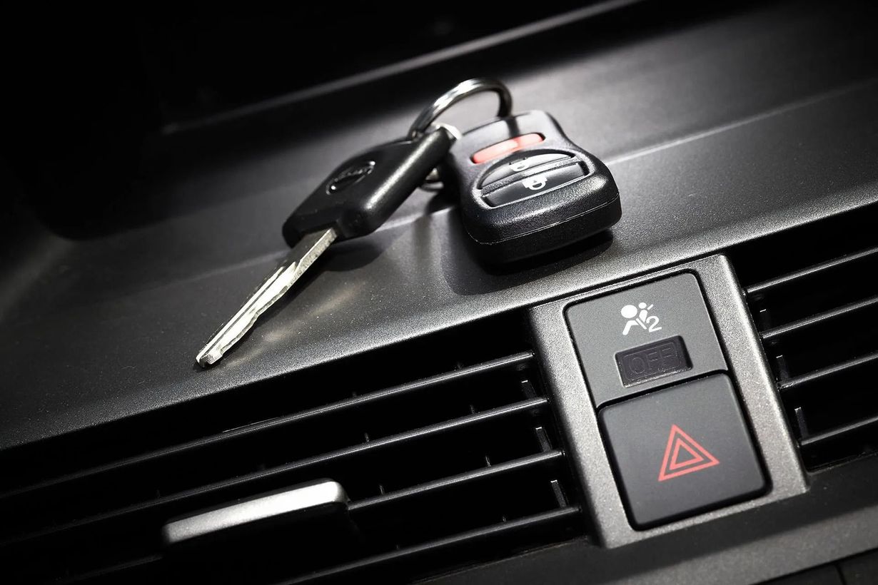 Car keys resting on a dashboard near an emergency hazard button.