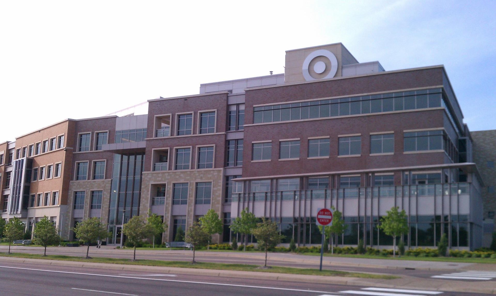 Multi-story modern brick building with large windows, near a street with trees.