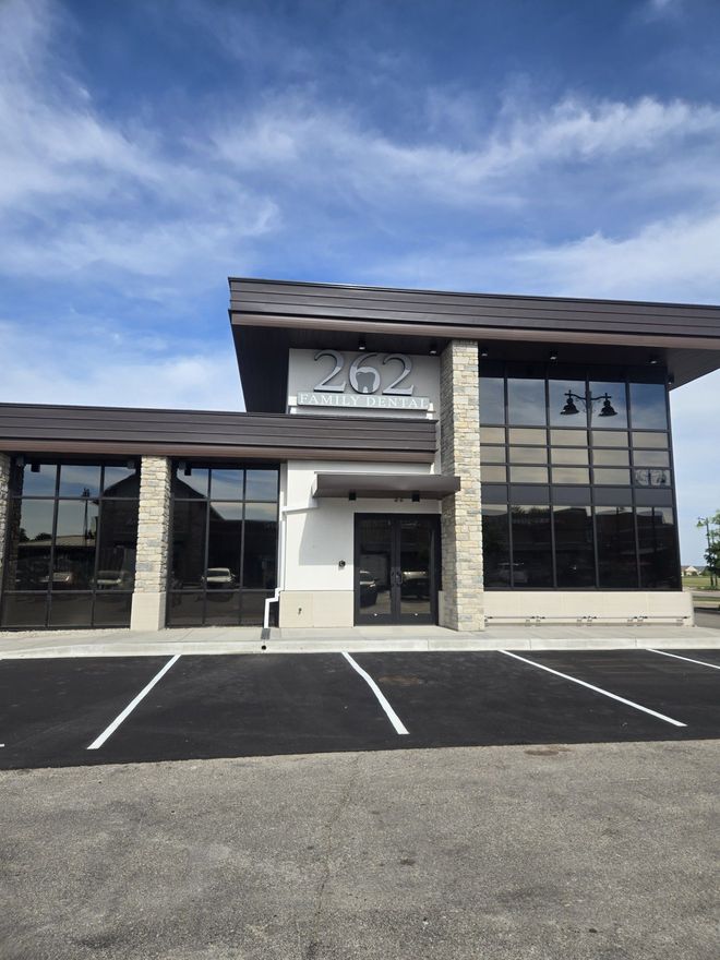 Modern commercial building with large windows and parking spaces in front under a blue sky