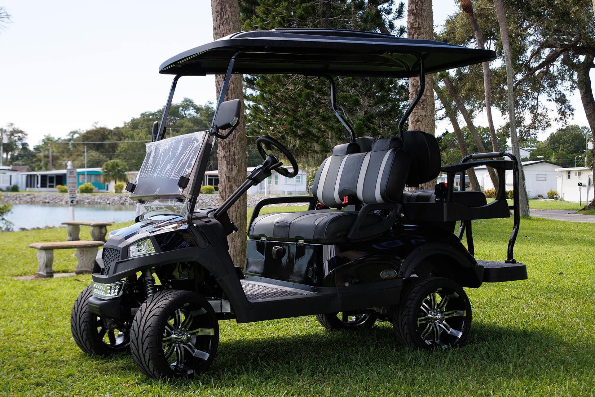 Black golf cart with upgraded wheels, seats, and canopy on green grass.