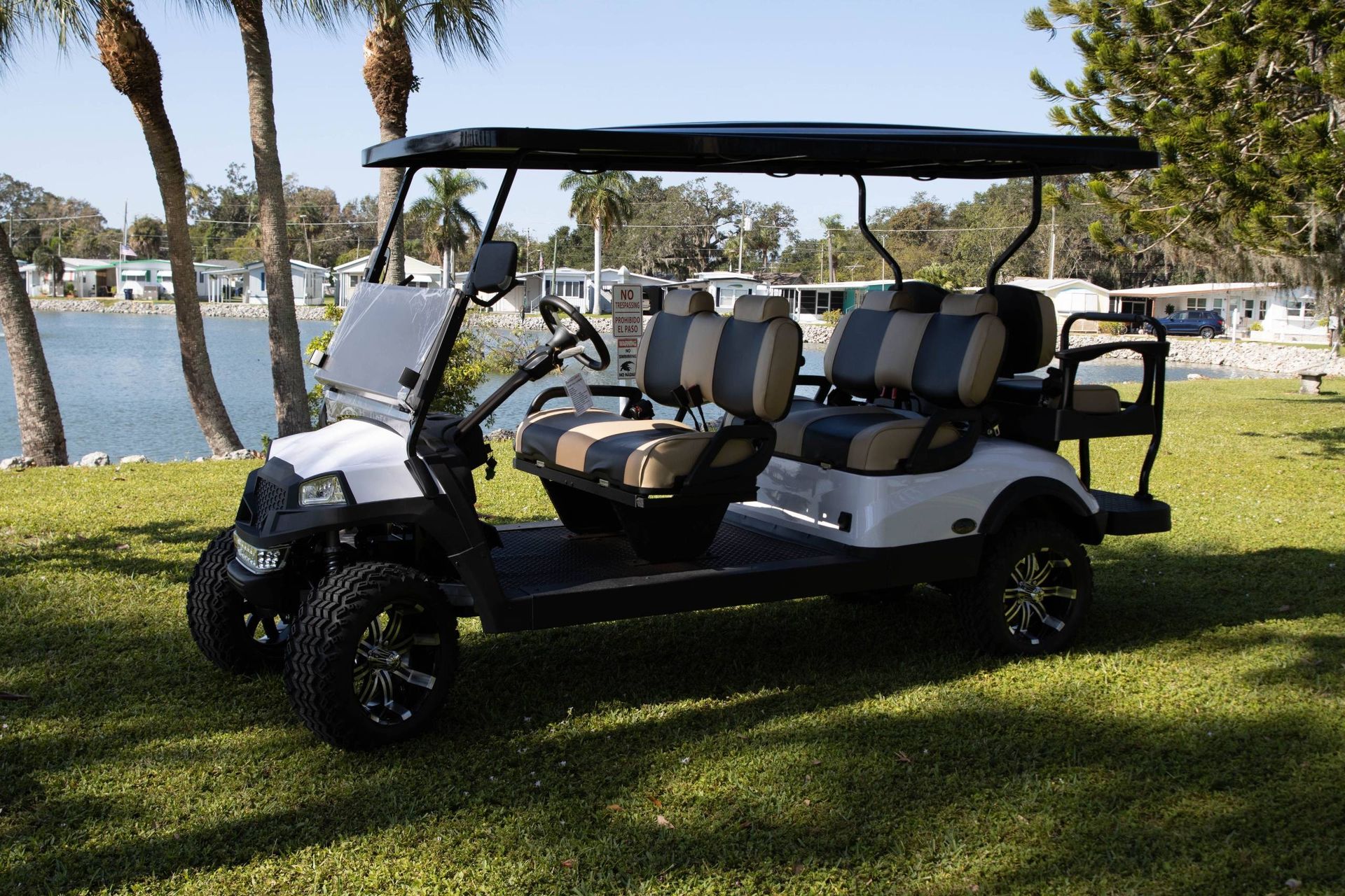 White golf cart with black accents, parked on grass near water and palm trees.