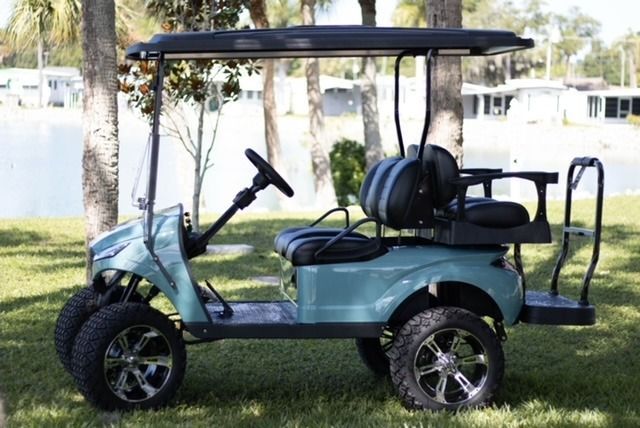 Blue golf cart with black roof parked on grass near water.